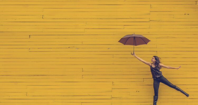 woman holding a brown umbrella against a yellow brick wall